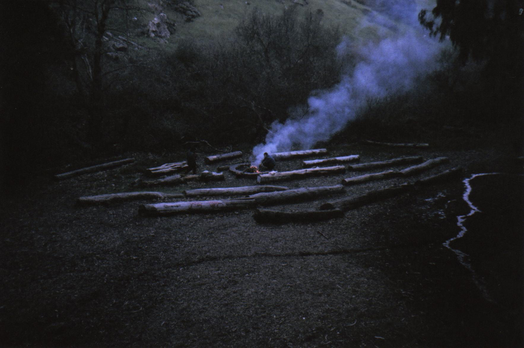 column of smoke in the woods as two figures build a fire