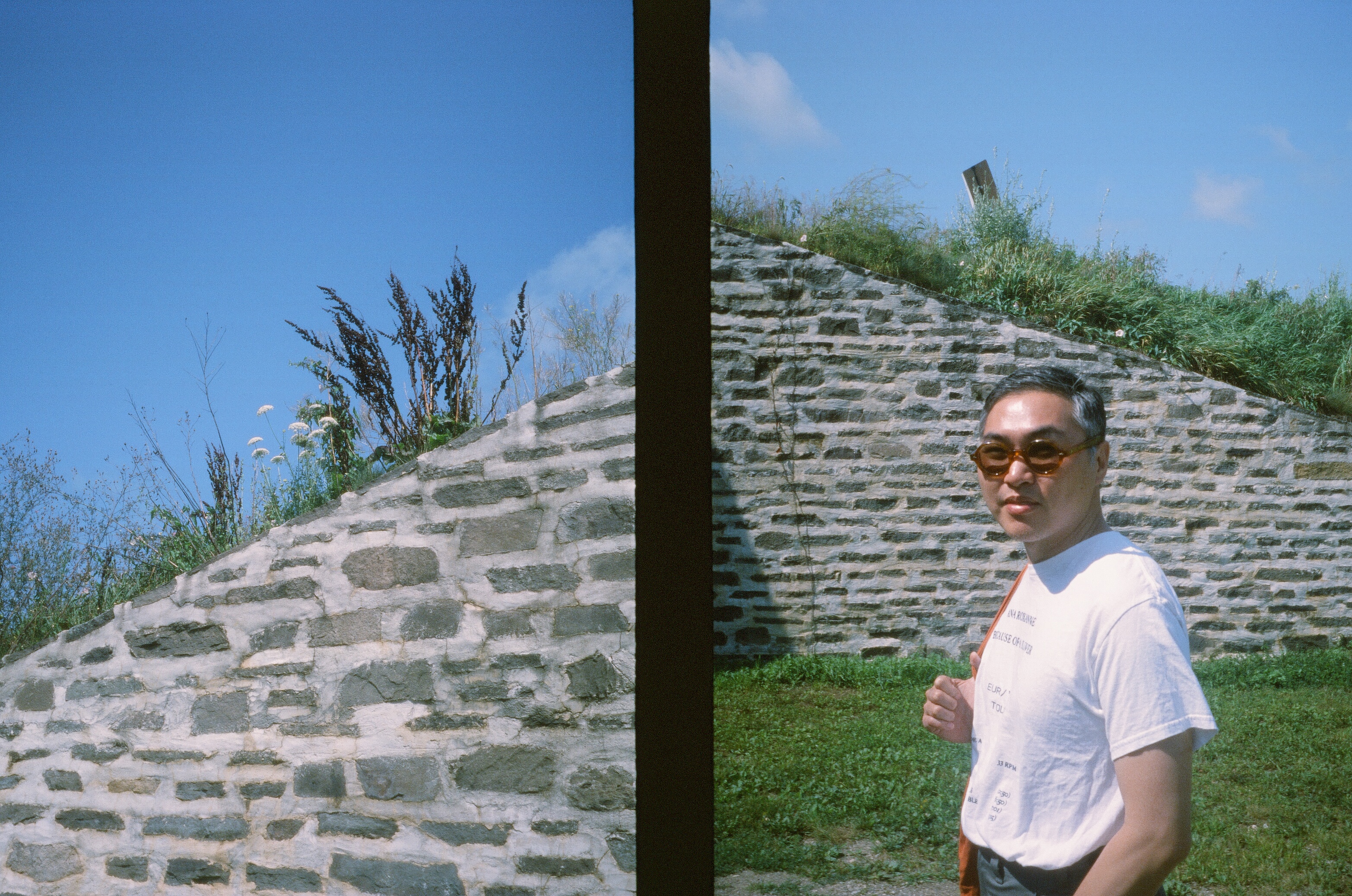 someone wearing sunglasses stands next to a stone wall