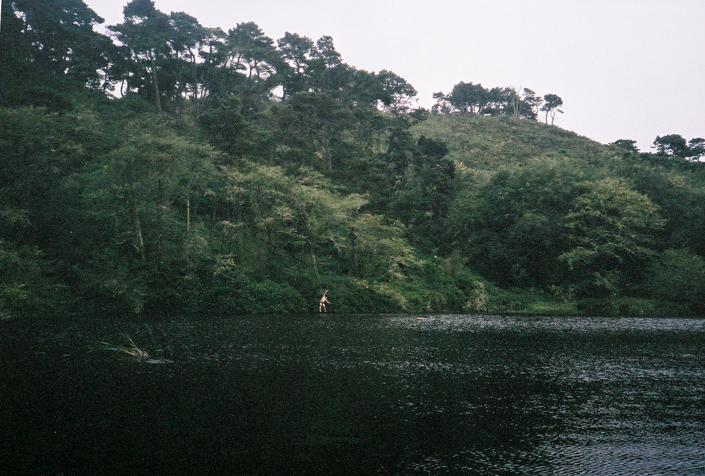 person in distance swinging on a rope into a lake